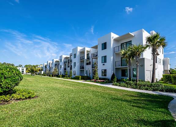 A row of white apartment buildings with green lawns in front.