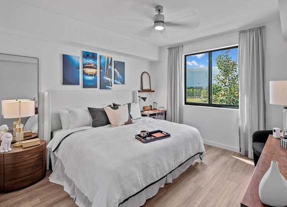 A bedroom with a large bed, a ceiling fan, and a view of the outdoors through a window.