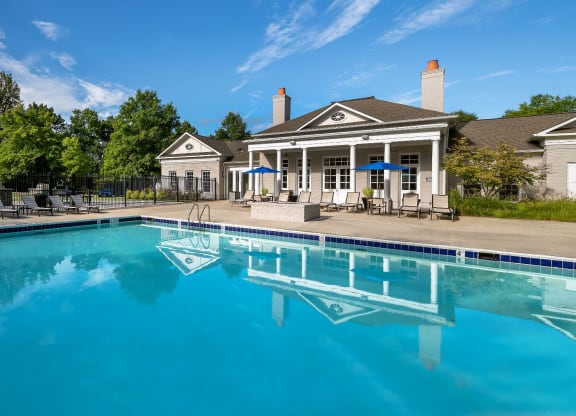 a swimming pool with lounge chairs and umbrellas in front of a house