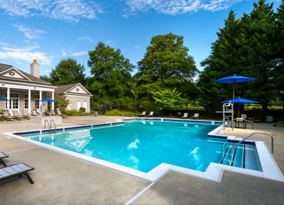a swimming pool with lounge chairs and umbrellas in front of a house