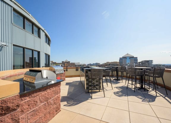 a rooftop patio with tables and chairs and a city in the background