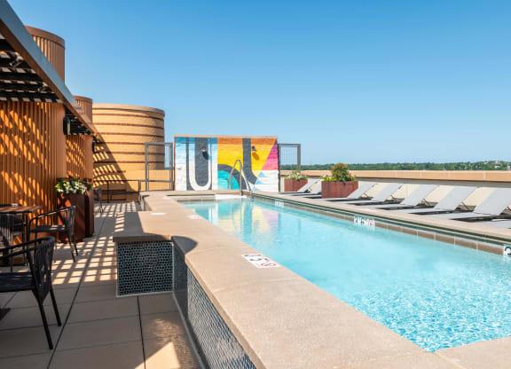 a swimming pool on the rooftop of a hotel with chairs around it