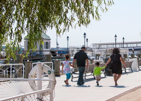 A family of three walks down a sidewalk past a no parking sign.