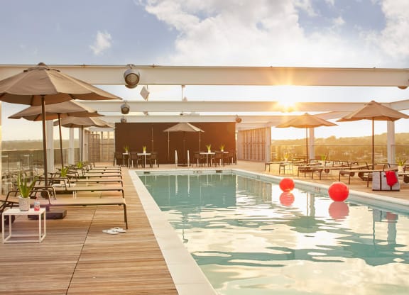 a swimming pool on the top of a building with chairs and umbrellas