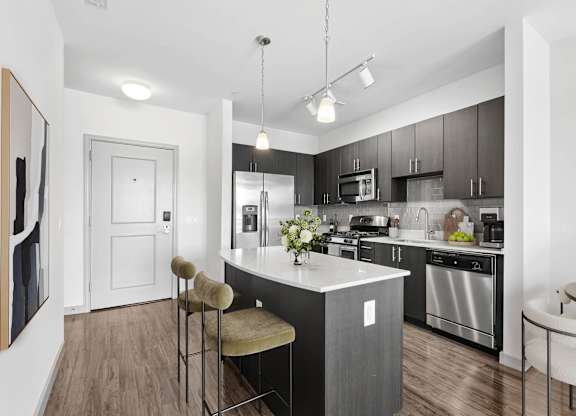 Kitchen at 7001 Arlington at Bethesda in Bethesda, MD, featuring quartz countertops, espresso cabinetry, a center island with seating, tile backsplash, and stainless-steel appliances.