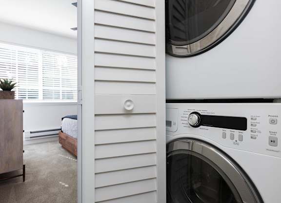 A washing machine is in the foreground of a laundry room.