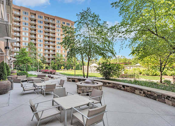 A patio with tables and chairs is surrounded by trees and a stone wall.