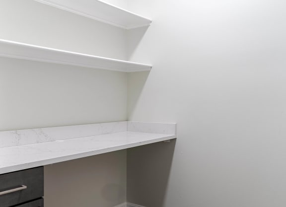 a corner of a room with white walls and a white counter top and a shelf