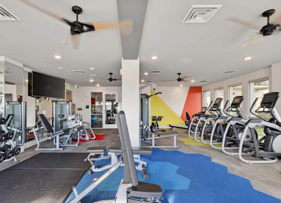Apartment fitness center with modern gym equipment and large windows.