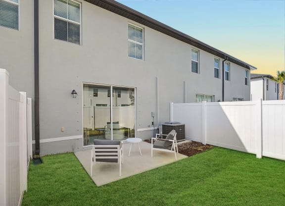 a patio with two chairs and a grill in front of a white building with a black roof