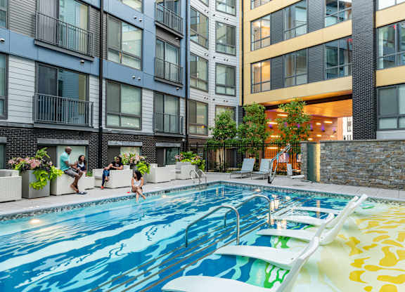 A swimming pool in a residential building with people relaxing by the poolside.