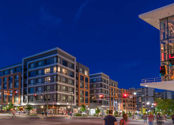 A city street at night with people walking and buildings with lit up windows.