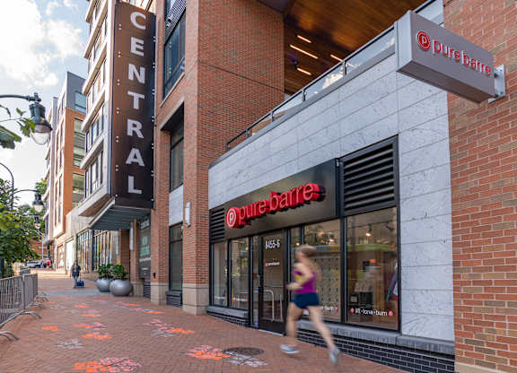 A woman runs past a Pure Barre studio on a city sidewalk.