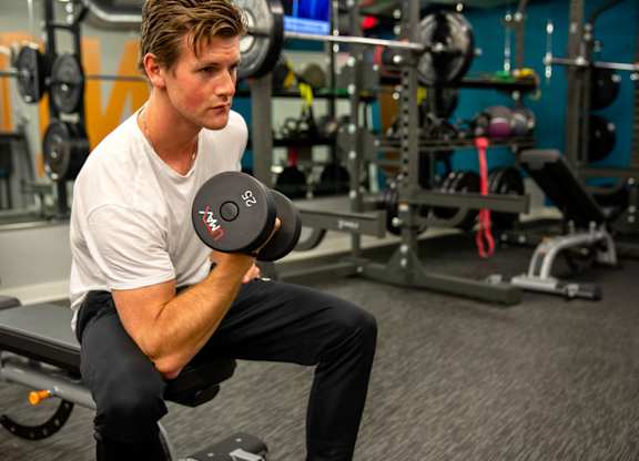 A man is sitting on a bench in a gym holding a dumbbell.