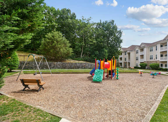 A playground with a swing set and a slide in the foreground and apartment buildings in the background.