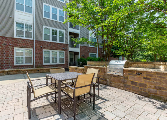 a patio with a table and chairs and a grill in front of a brick building