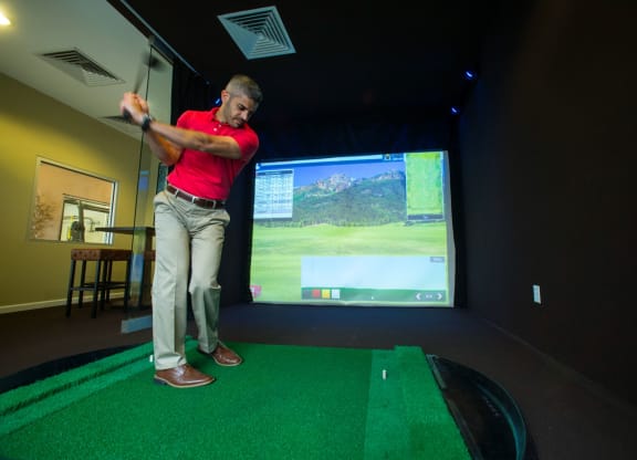 a man in a red shirt is swinging a golf club at a golf ball