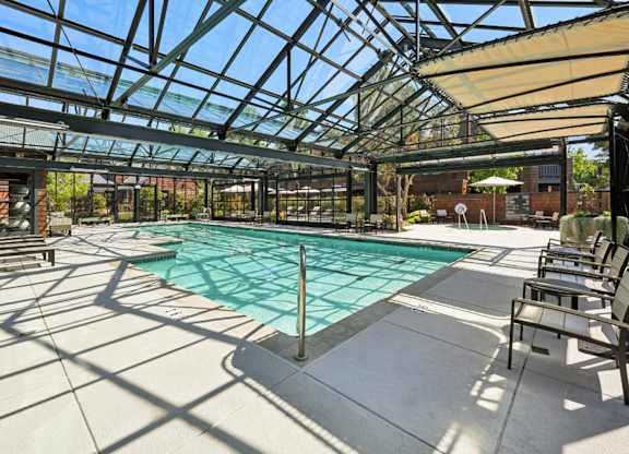 Indoor swimming pool with glass enclosure, lounge chairs, and natural sunlight.