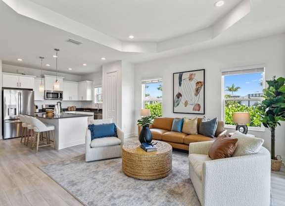 A modern living room with a white sofa, a grey rug, and a kitchen in the background at Marisol in Lakewood Ranch, FL
