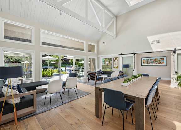 Clubhouse dining area with long wood table, blue accent mural wall, and adjacent kitchen