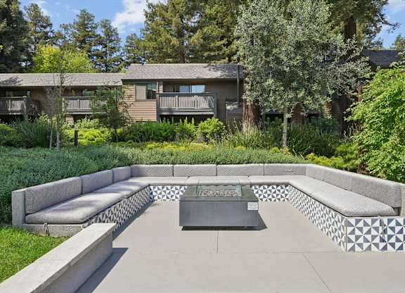 Outdoor fire pit with built-in seating and surrounding greenery at Old Orchard Apartments