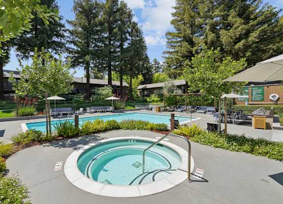Outdoor hot tub with surrounding seating, landscaping, and pool area at Old Orchard Apartments