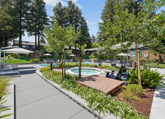 Pool area with hot tub, lounge chairs, umbrellas, and landscaped greenery