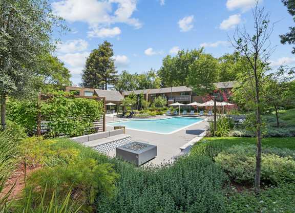 Pool area at Old Orchard Apartments surrounded by lush landscaping and outdoor seating.