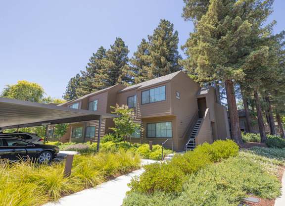 Apartment building exterior with landscaped walkway, covered parking, and surrounding trees