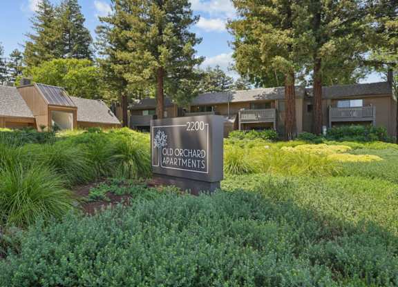 Entrance sign for Old Orchard Apartments surrounded by mature trees and landscaped grounds.