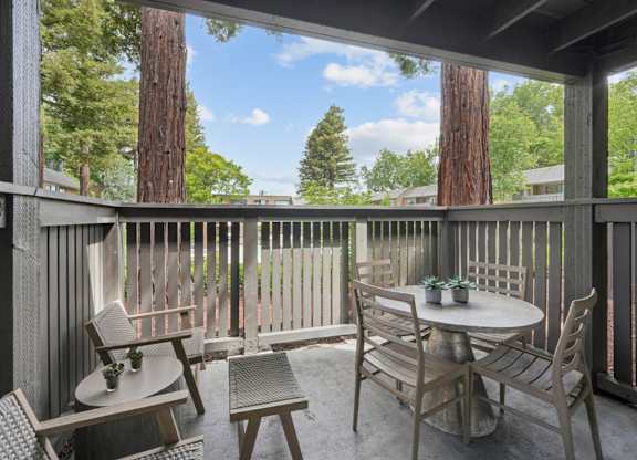 Private patio with seating and table overlooking trees at Old Orchard Apartments