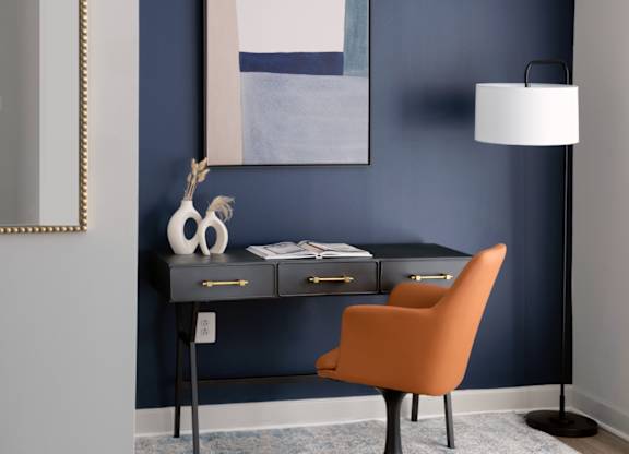 A desk with a chair and a lamp in front of a blue wall.