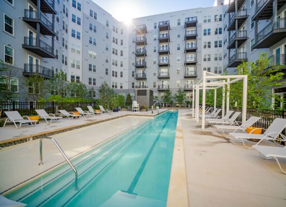 a pool with lounge chairs next to an apartment building