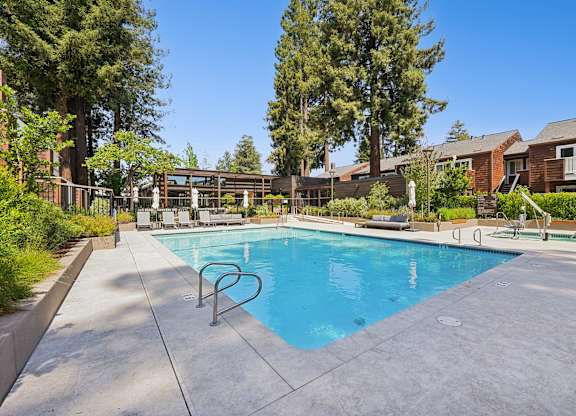 A swimming pool surrounded by trees and a building in the background.