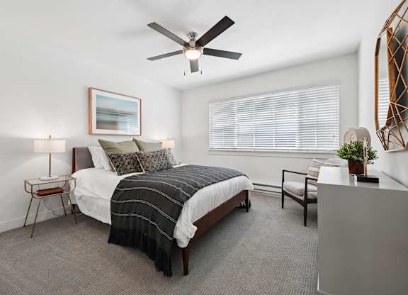 A bedroom with a bed, chair, and a ceiling fan.