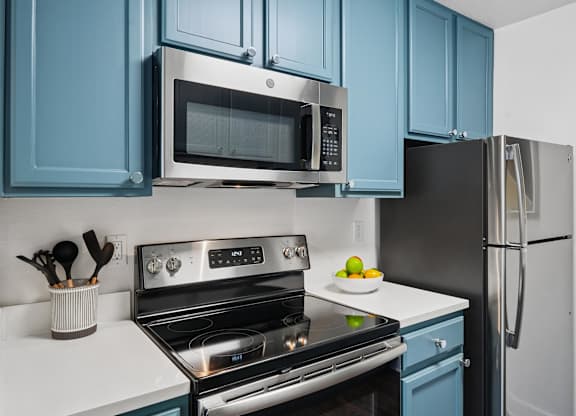A kitchen with blue cabinets and a stainless steel oven and microwave.