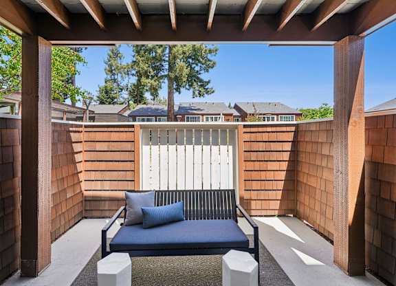 A blue couch is on a patio with a white fence in the background.