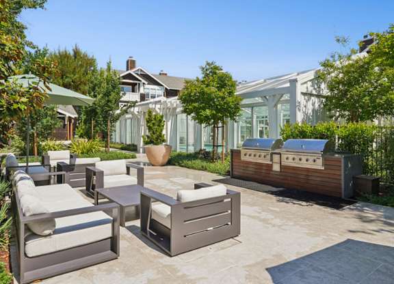 Outdoor grilling and lounge area at Pescadero Apartments with patio seating, landscaped surroundings, and poolside access.
