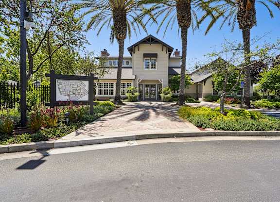 A street view with a house, palm trees, and a sign.