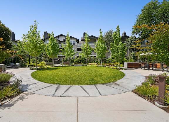 A large grassy area surrounded by trees and a concrete walkway in front of a building.