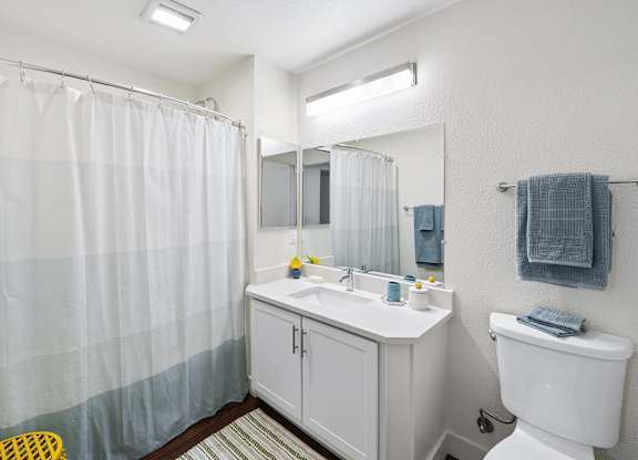 A white bathroom with a white toilet, sink, and shower curtain.