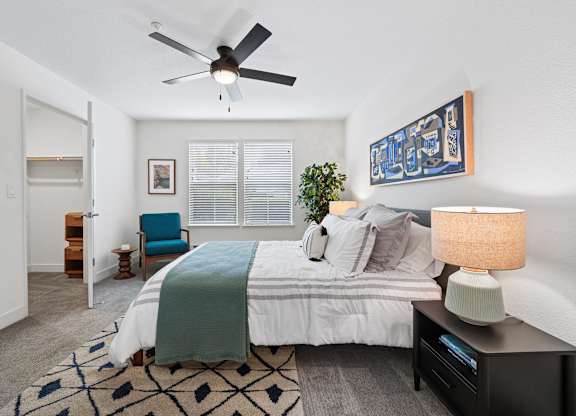 A bedroom with a bed, a chair, a ceiling fan, and a rug.