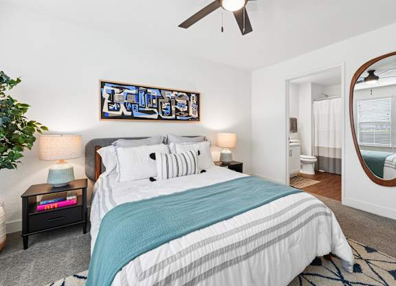 A bedroom with a bed, a ceiling fan, and a mirror.