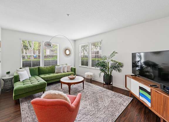 A living room with a green couch, a red chair, and a television.