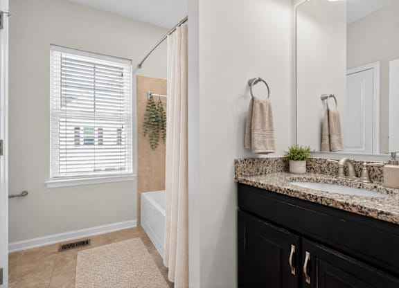 Bathroom with bathtub and shower, granite countertop, and window with blinds.