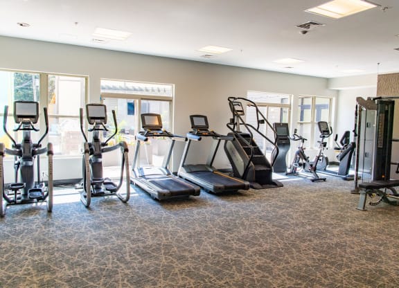 a gym with cardio equipment in a room with windows