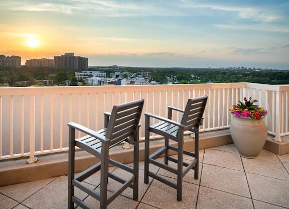 Two chairs are on a balcony with a sunset view.