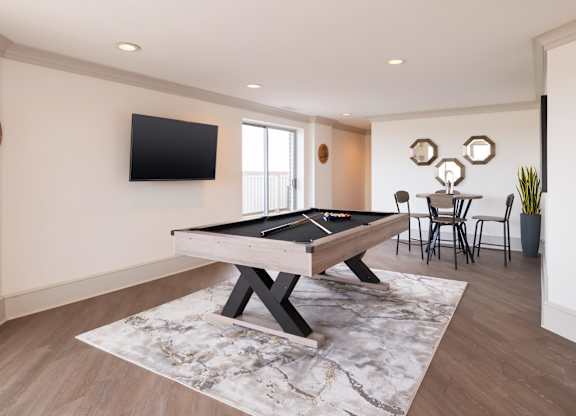 A pool table is in the middle of a room with a TV mounted on the wall.