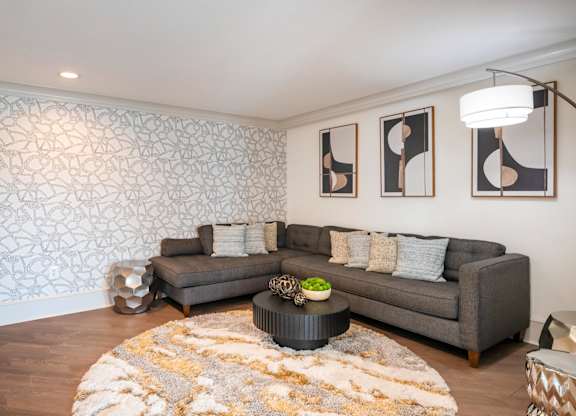 A living room with a grey couch, a coffee table, and a patterned wallpaper.