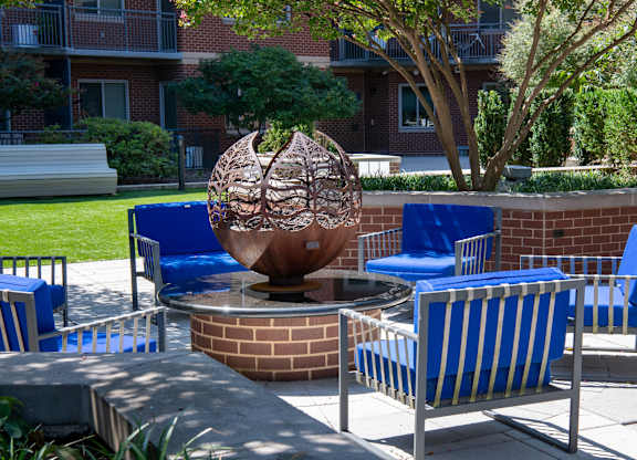 Close view of a spherical metal fire feature surrounded by blue cushioned chairs in the landscaped courtyard.